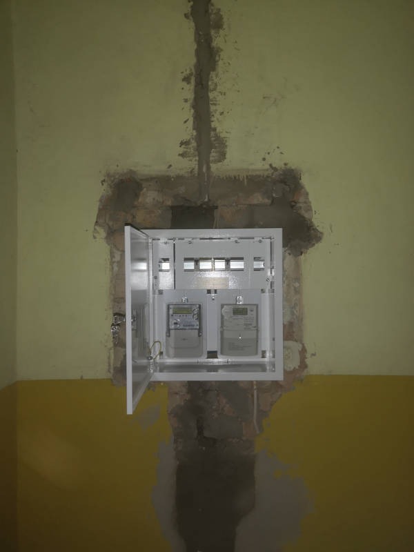 Otwarta skrzynka z dwoma licznikami elektrycznymi zamontowana w ścianie z widocznymi śladami prac murarskich i niedomalowaną ścianą w dwóch kolorach.