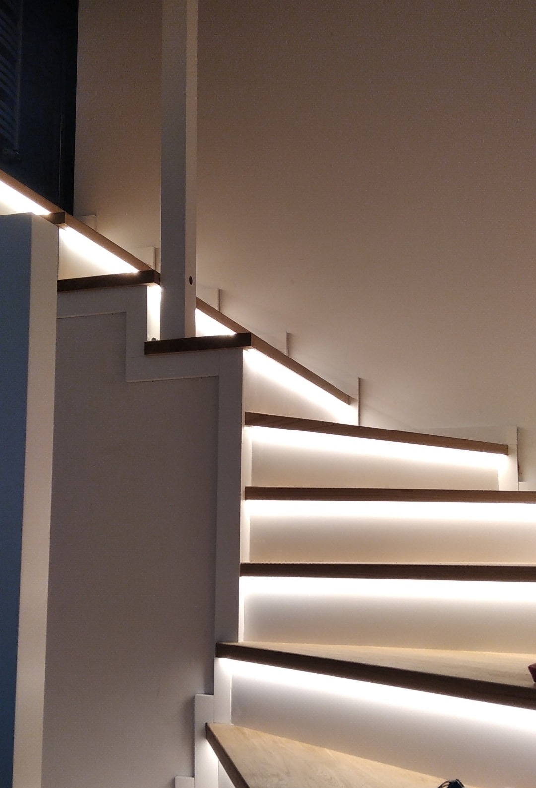 Nowoczesne schody z podświetleniem LED w Białymstoku, z drewnianymi stopniami i białymi podstopnicami, oświetlone ciepłym, białym światłem.
