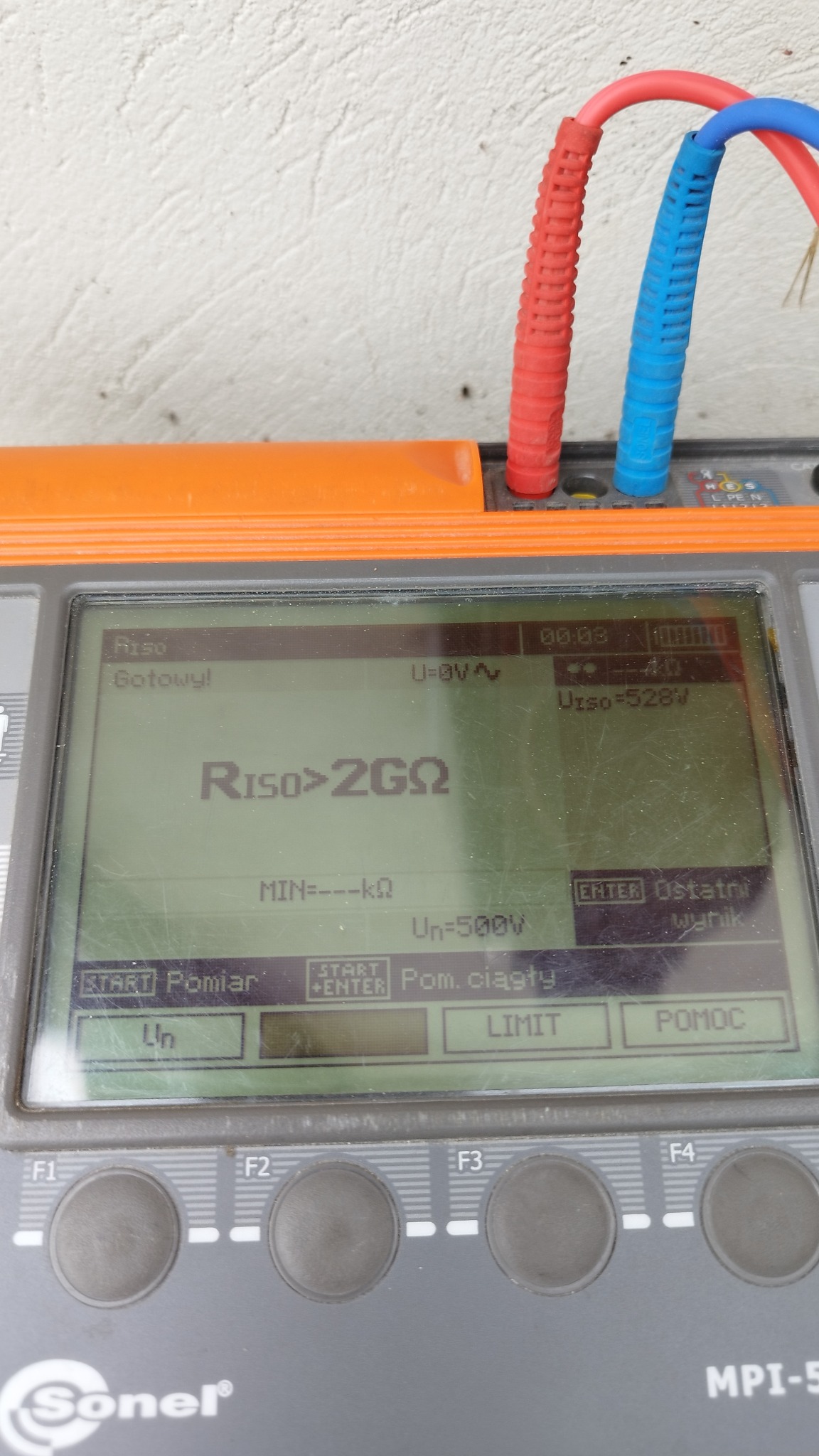 Miernik Sonel MPI-528 z podłączonymi przewodami pomiarowymi, wyświetlający wynik pomiaru rezystancji izolacji powyżej 2 Gigaomy przy napięciu 500V. Widoczny ekran urządzenia z tekstem 'Riso>2GQ'...