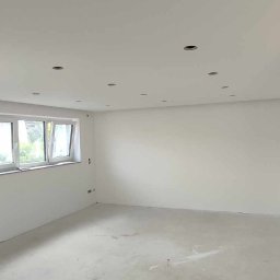 Wall Done Olaf Karbowniczek - Pokój po szpachlowaniu i gładziowaniu, z przygotowanymi otworami na oświetlenie punktowe w suficie, widoczne okno.
