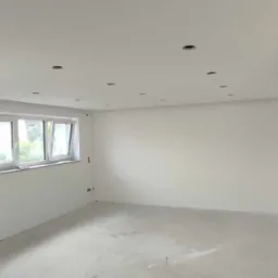 Pokój po szpachlowaniu i gładziowaniu, z przygotowanymi otworami na oświetlenie punktowe w suficie, widoczne okno.