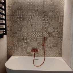 Wall Done Olaf Karbowniczek - Wykończona łazienka z wanną, mozaiką na ścianie i miedzianą armaturą. Podświetlenie LED nadaje wnętrzu nowoczesny charakter. Grzejnik drabinkowy po lewej stronie.