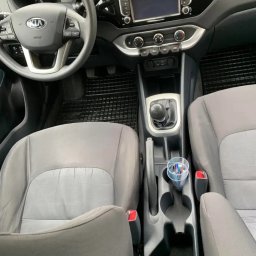 Bomba Garage Auto Detailing - Wnętrze samochodu marki Kia, widok z przodu, obejmujący deskę rozdzielczą, kierownicę, fotele i tunel środkowy z uchwytem na napoje zawierającym długopisy.