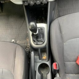 Bomba Garage Auto Detailing - Wnętrze samochodu przed czyszczeniem: brudna konsola środkowa, widoczne okruchy i kurz na fotelach, gałka zmiany biegów oraz panel sterowania klimatyzacją.