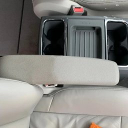 Bomba Garage Auto Detailing - Czyszczenie jasnej skórzanej tapicerki samochodowej: widoczna różnica przed i po na podłokietniku, z pomarańczową ściereczką w tle.