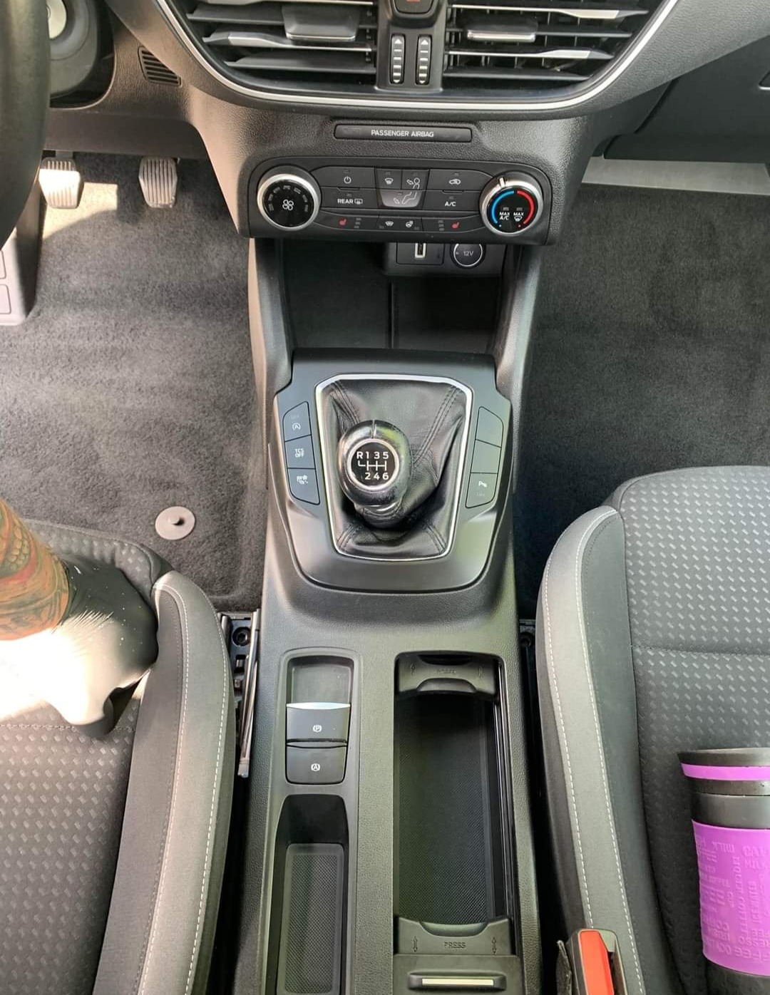 Wnętrze samochodu z manualną skrzynią biegów, widok z góry na konsolę środkową, z widocznym lewarkiem zmiany biegów, panelem klimatyzacji i fragmentami foteli.