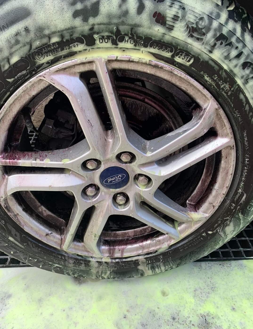 Koło samochodu Ford pokryte pianą myjącą i śladami płynu do czyszczenia felg, widoczne tarcze hamulcowe.