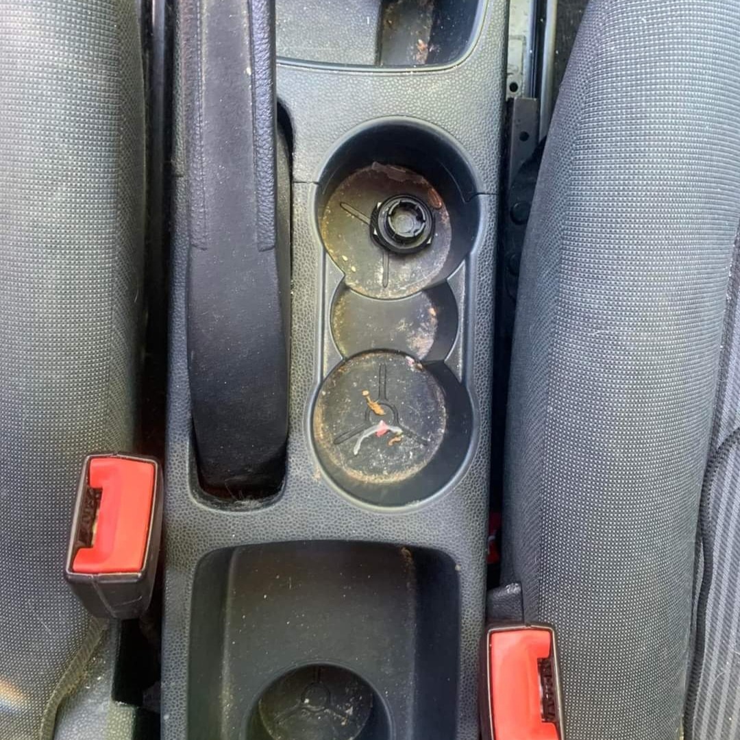 Brudny, zaniedbany schowek samochodowy z uchwytami na napoje, widoczne resztki płynów i kurzu, zapuszczone wnętrze pojazdu.