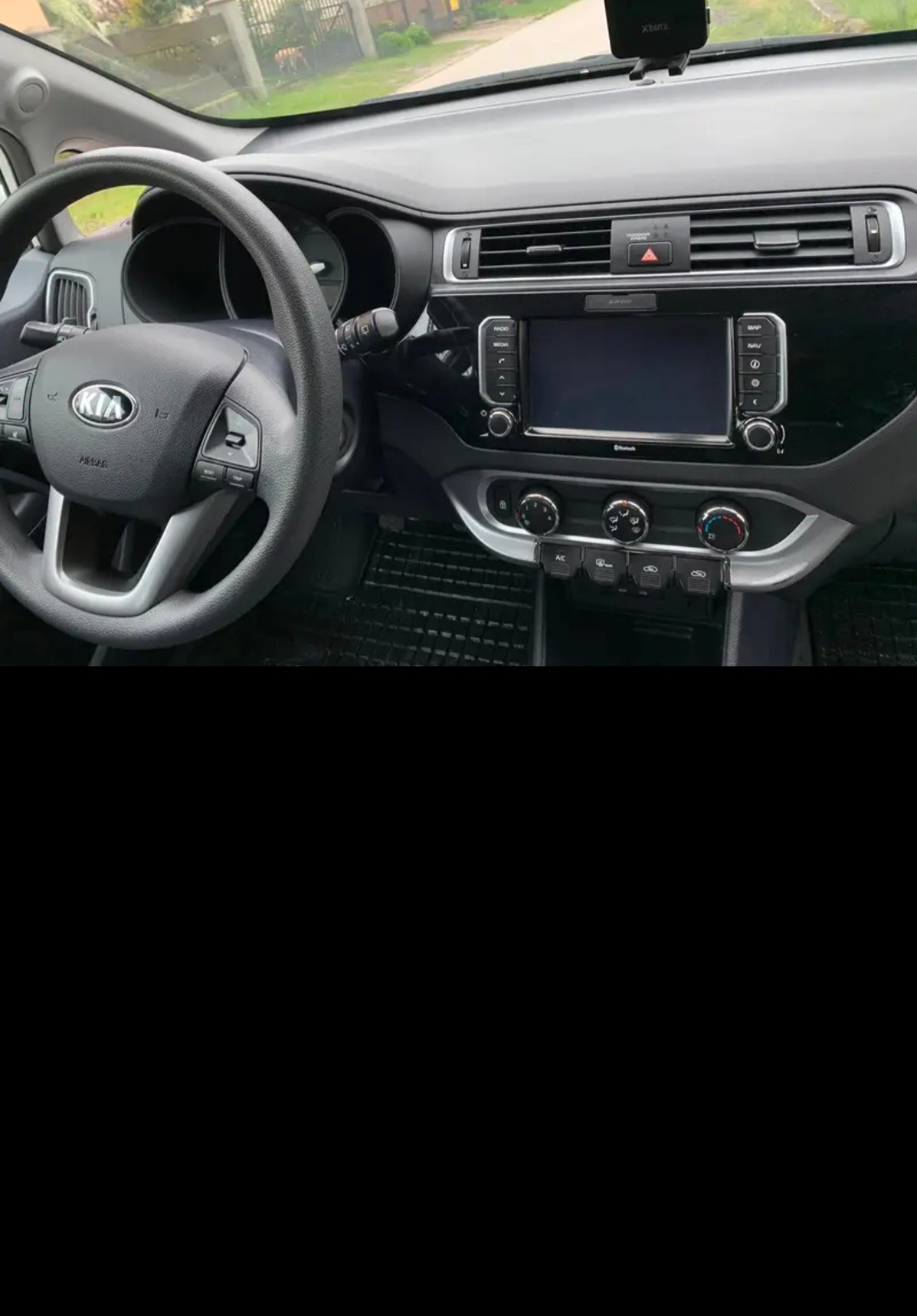 Wnętrze samochodu Kia Rio: deska rozdzielcza z radiem, klimatyzacją i kierownicą z logo Kia, widok z perspektywy kierowcy.
