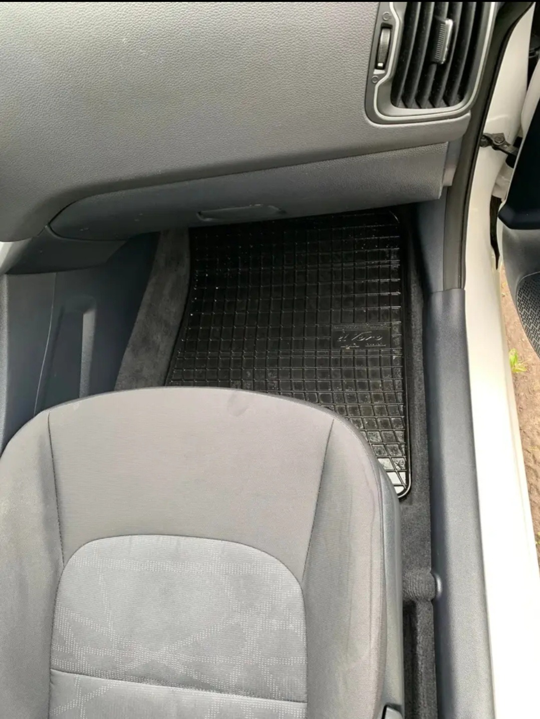 Wnętrze samochodu z widocznym szarym fotelem i czarnym gumowym dywanikiem pod nogami kierowcy.