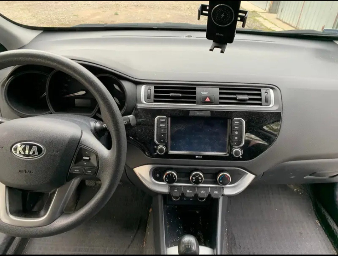 Wnętrze samochodu marki Kia z widoczną deską rozdzielczą, kierownicą z logo, panelem sterowania i uchwytem na telefon.