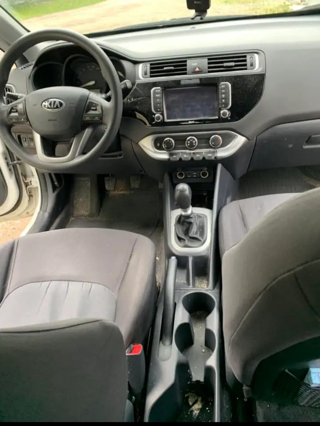 Wnętrze samochodu marki Kia z widocznym kokpitem, kierownicą z logo, deską rozdzielczą z ekranem i brudnymi fotelami oraz konsolą środkową.