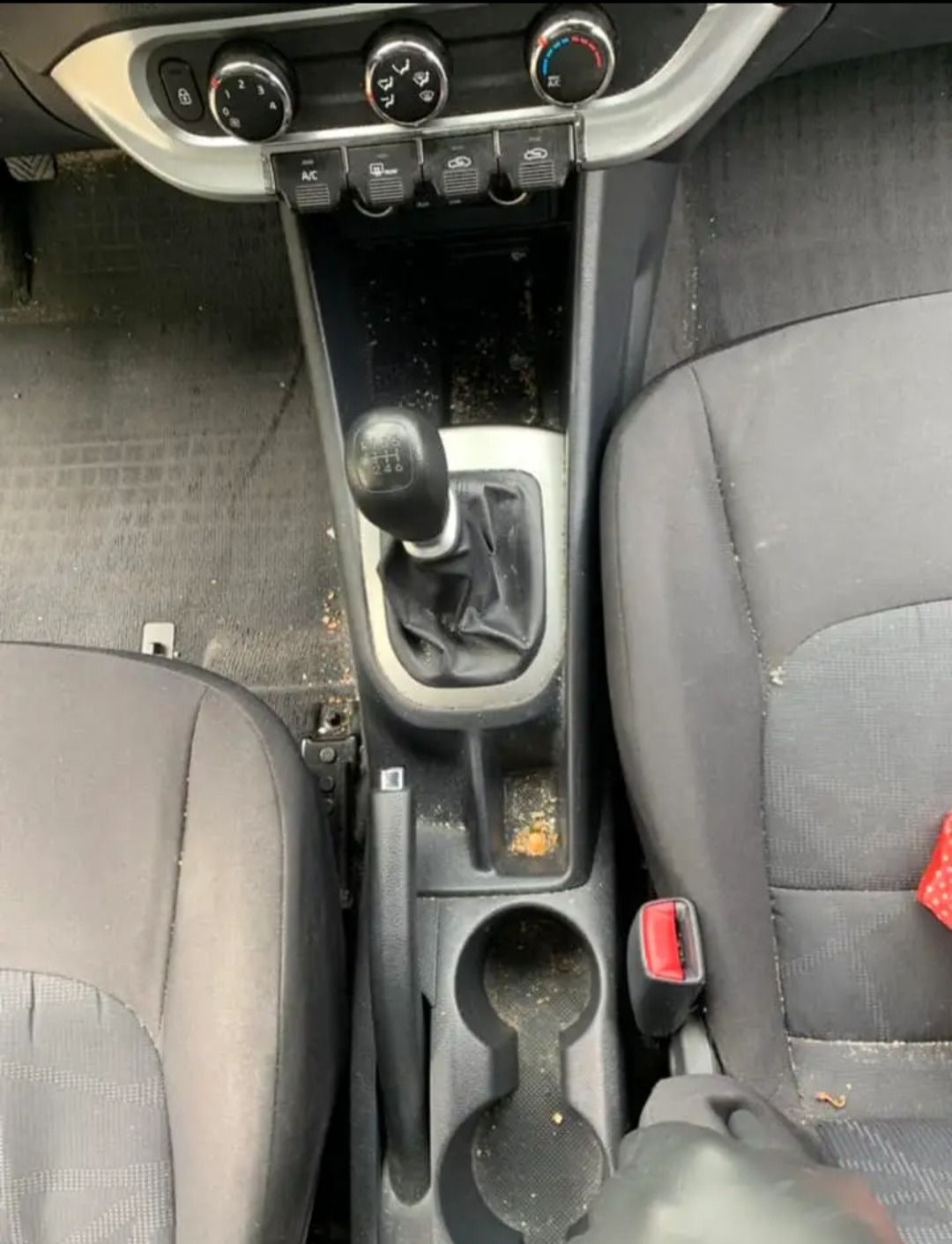 Wnętrze samochodu przed czyszczeniem: brudna konsola środkowa, widoczne okruchy i kurz na fotelach, gałka zmiany biegów oraz panel sterowania klimatyzacją.
