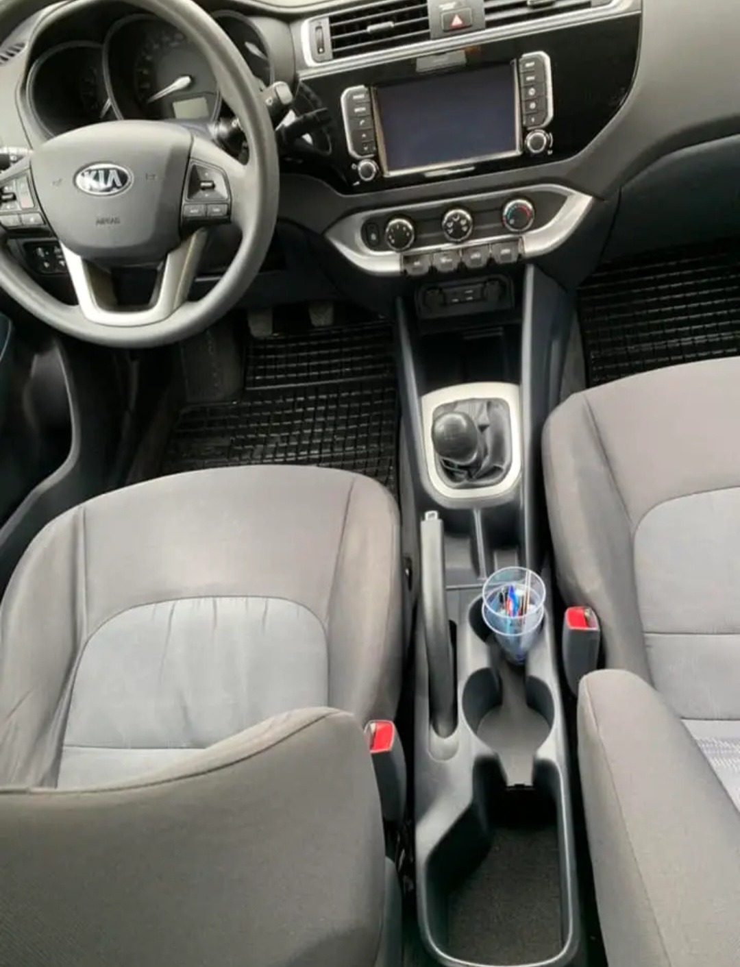 Wnętrze samochodu marki Kia sfotografowane w Piasecznie, z widocznymi szarymi fotelami, deską rozdzielczą i kubkiem z długopisami w uchwycie.