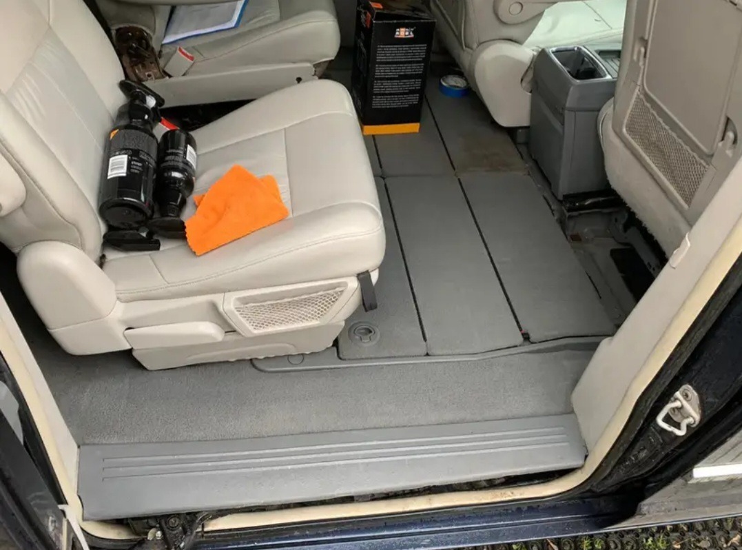 Wnętrze samochodu typu van w trakcie czyszczenia: widoczne środki czyszczące na skórzanym siedzeniu i pomarańczowa ściereczka z mikrofibry.
