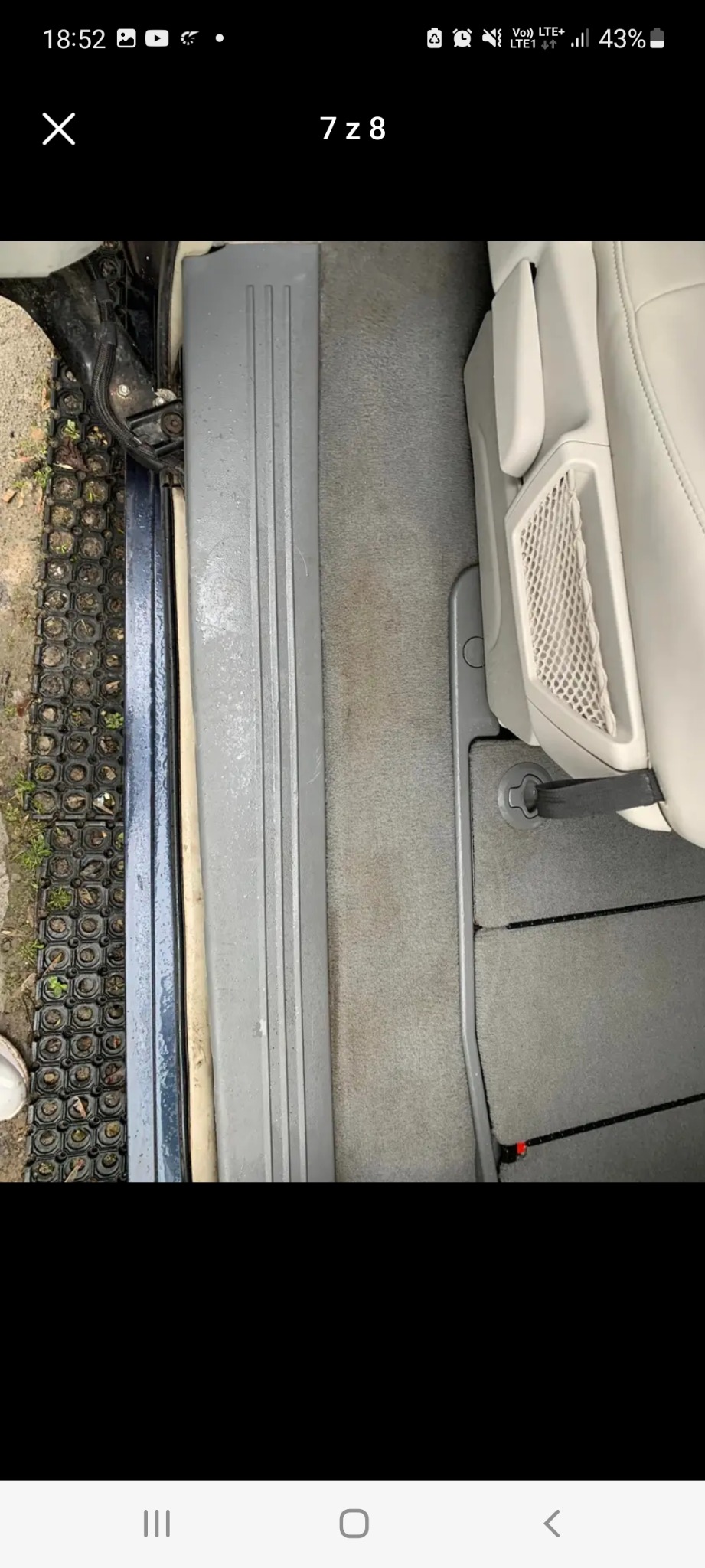 Wnętrze samochodu z widocznymi zabrudzeniami na dywaniku i progu, obok gumowa wycieraczka z drobnymi zanieczyszczeniami.