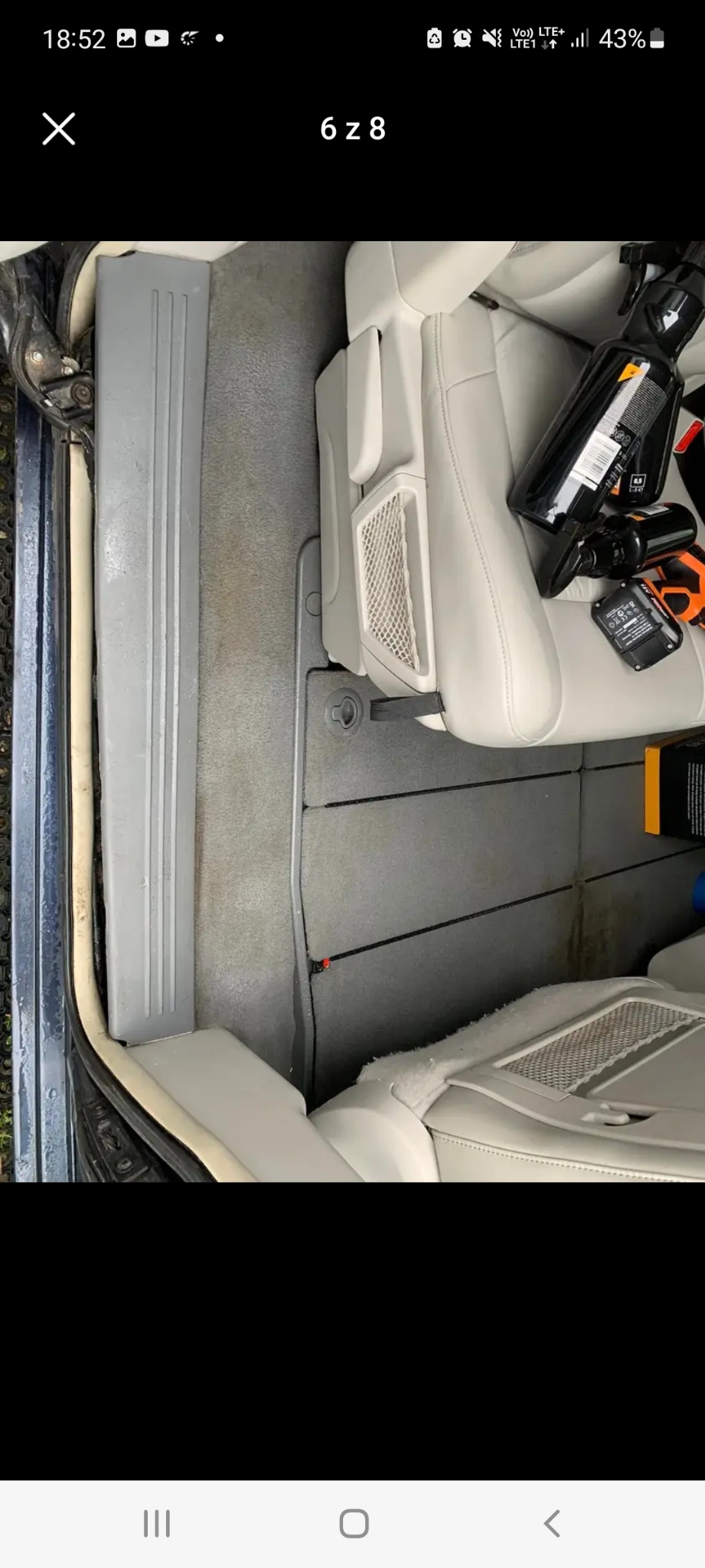 Wnętrze samochodu z jasną skórzaną tapicerką, widoczne butelki z preparatami do czyszczenia i akcesoria na siedzeniu, dywaniki częściowo zabrudzone.