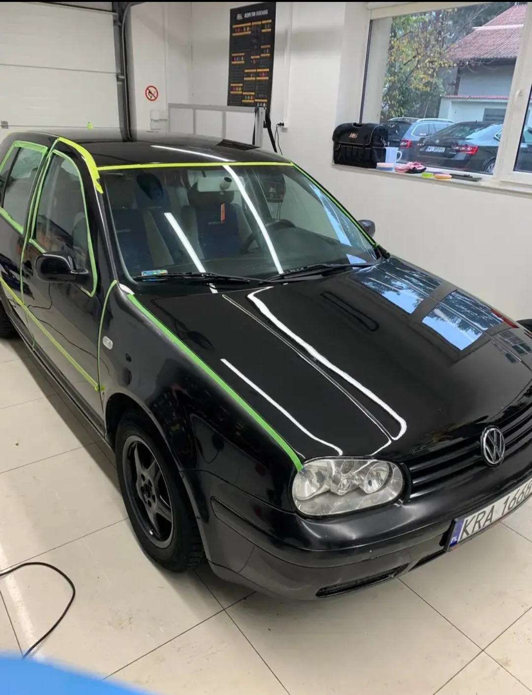 Czarny samochód Volkswagen Golf IV przygotowywany do oklejania, z zieloną taśmą maskującą wokół szyb i elementów karoserii, widoczne tablice rejestracyjne KRA 16668.