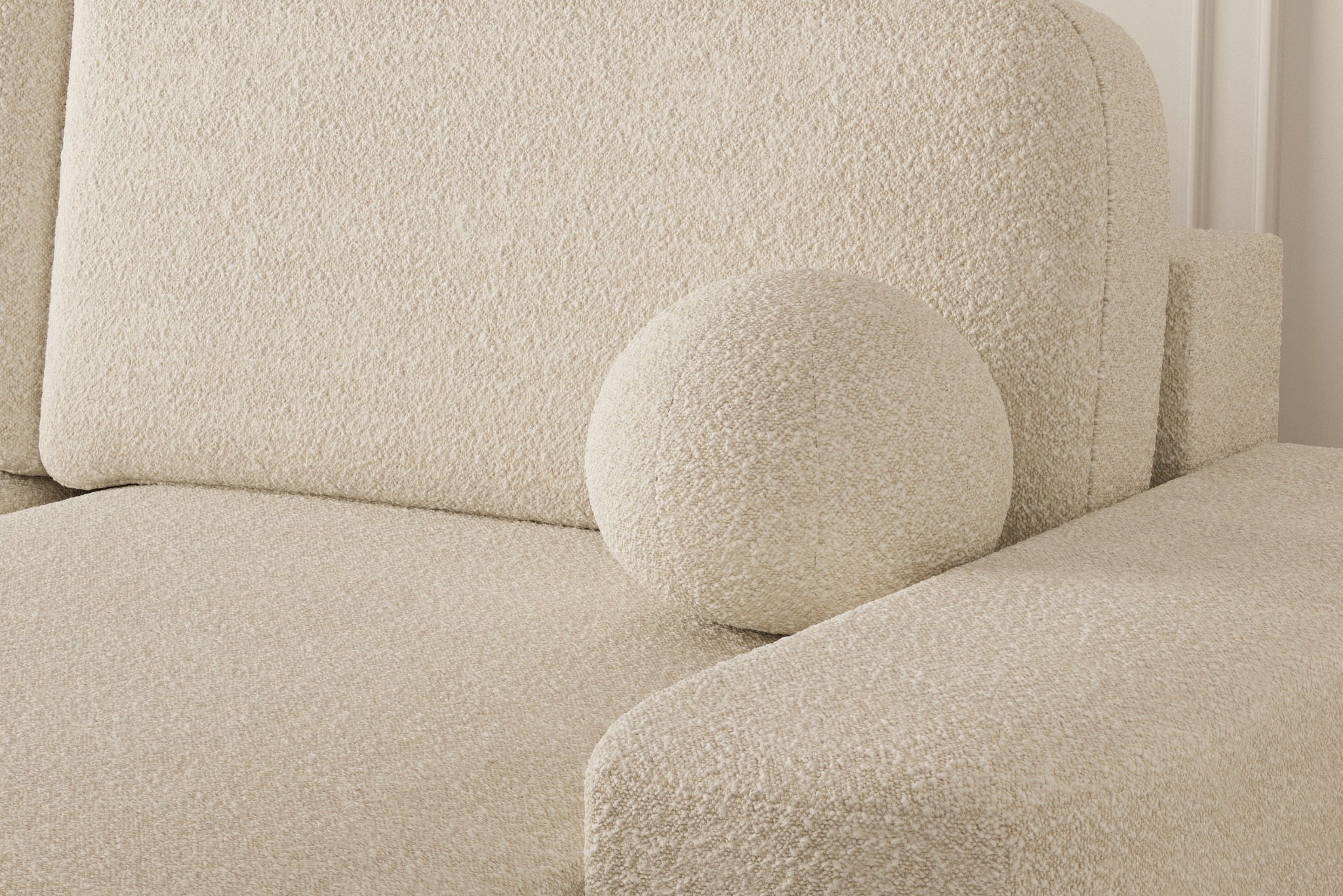 Fragment beżowej sofy z poduszką w kształcie kuli, wykonanej z grubej, teksturowanej tkaniny boucle.