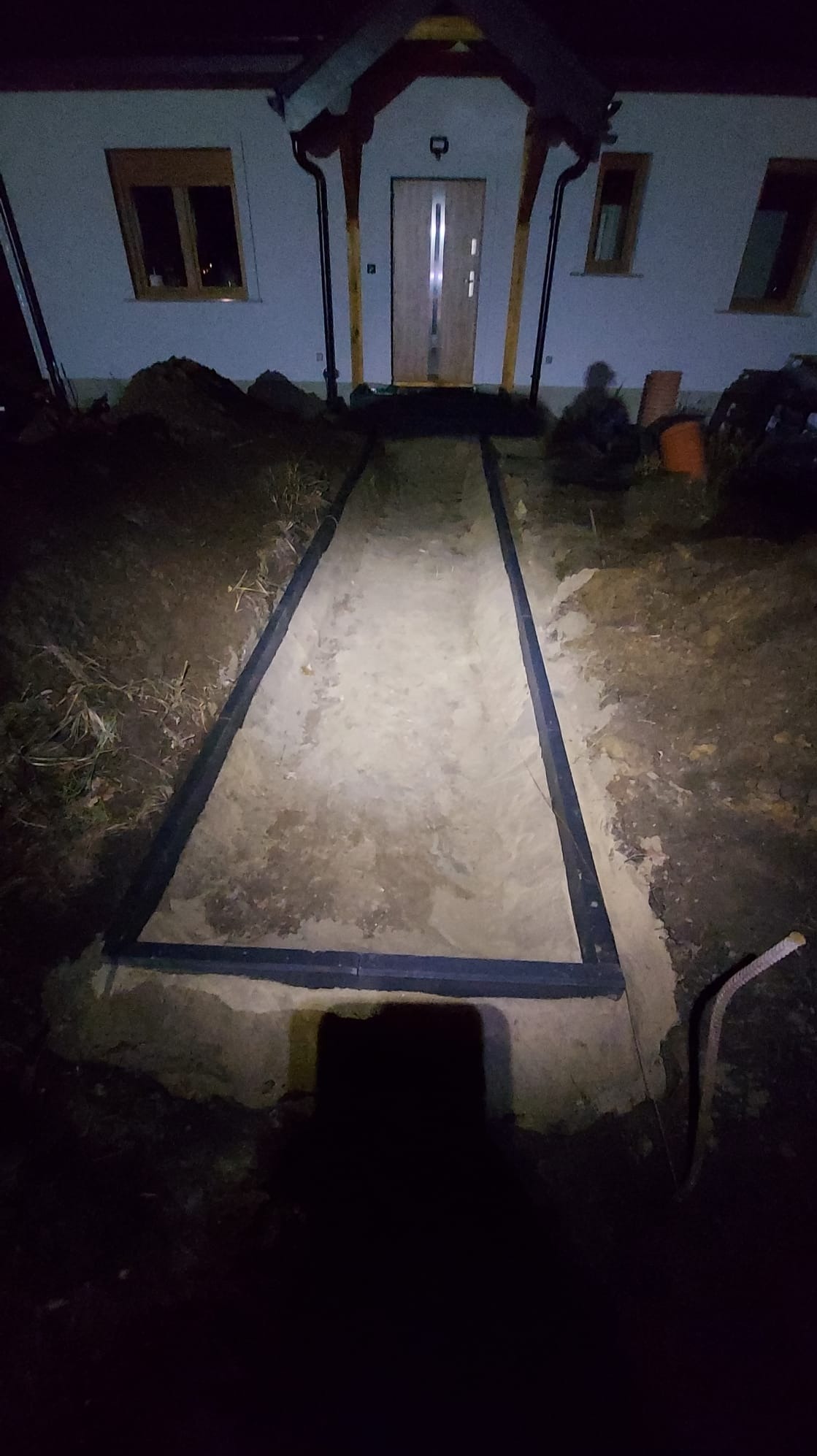 Przygotowany teren pod ścieżkę przed domem, z obramowaniem z tworzywa, piasek wyrównany, nocne oświetlenie.