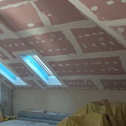 TARGET INC SPÓŁKA Z OGRANICZONĄ ODPOWIEDZIALNOŚCIĄ - Poddasze z oknami dachowymi w trakcie montażu płyt gipsowo-kartonowych, widoczne łączenia płyt wypełnione masą szpachlową. Elementy konstrukcyjne w tle.