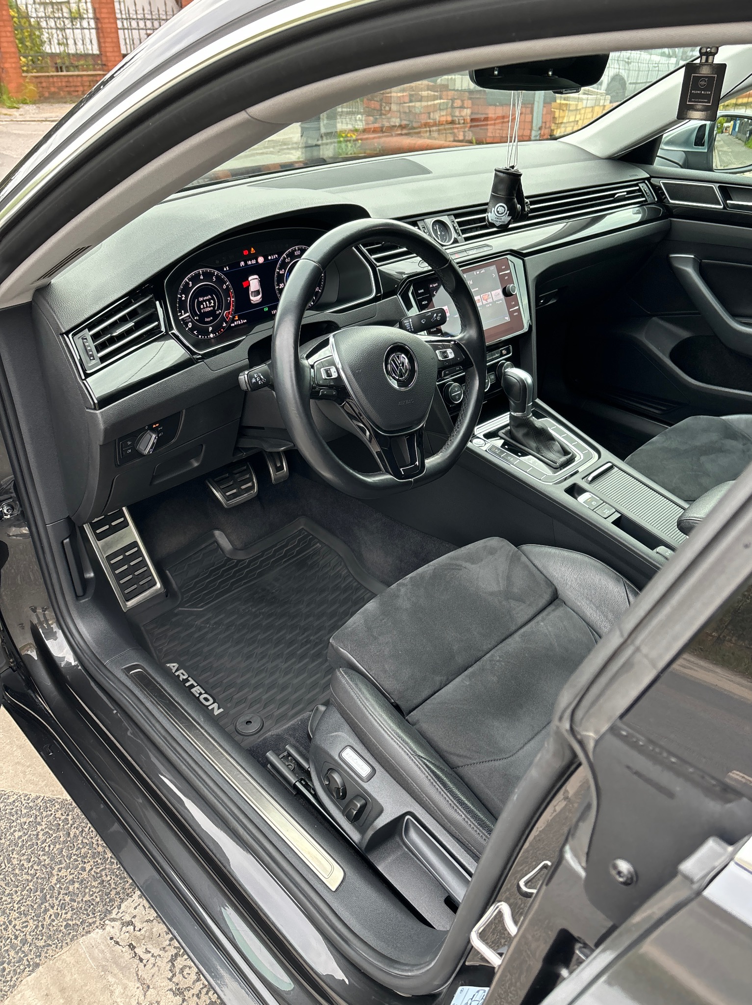 Wnętrze samochodu Volkswagen Arteon z czarną skórzaną tapicerką, widoczne detale deski rozdzielczej, kierownicy i dywaników z logo Arteon.