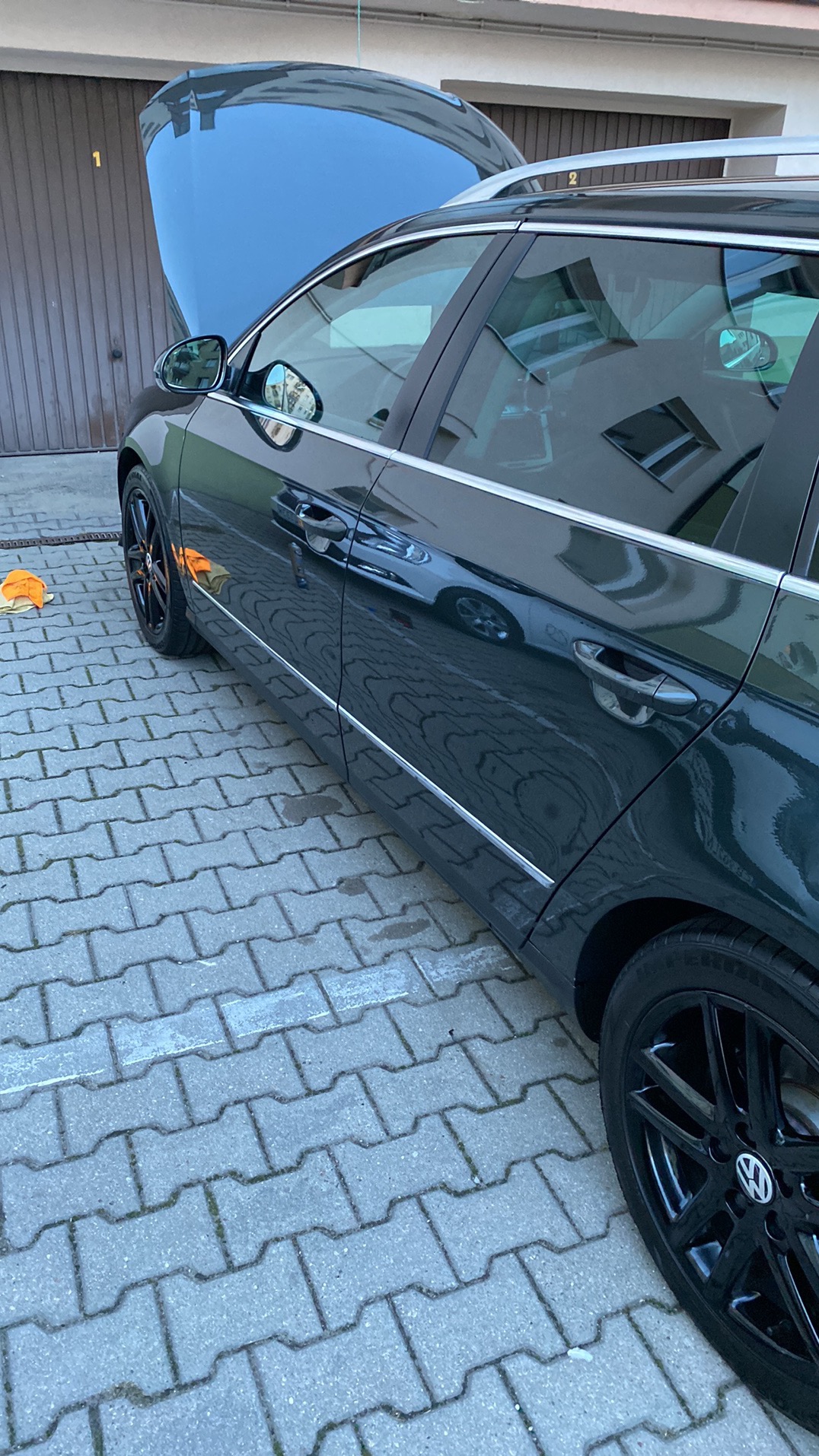 Ciemnozielony samochód kombi z otwartą maską, zaparkowany na kostce brukowej, widoczna pomarańczowa ściereczka do polerowania.