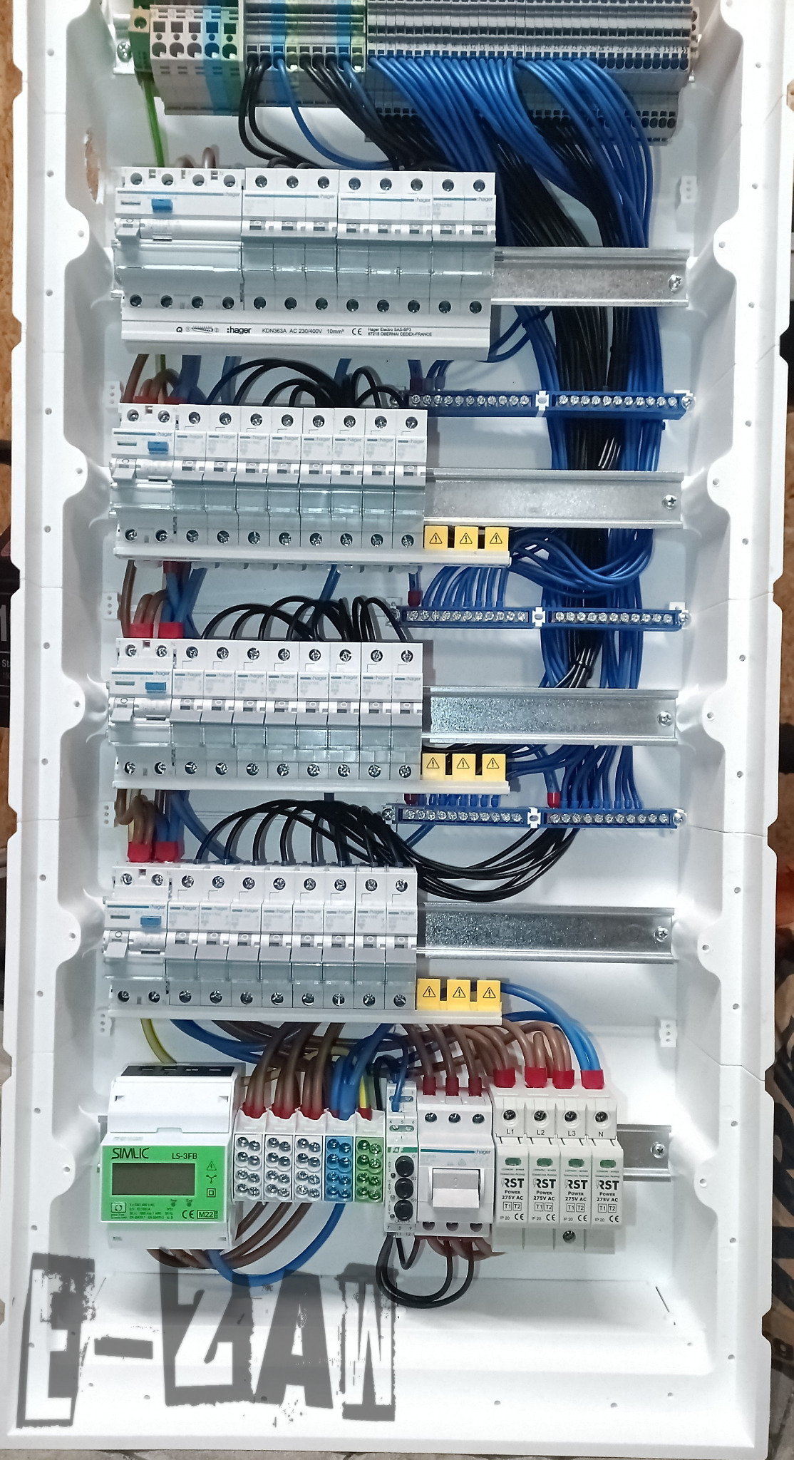 Rozdzielnica elektryczna z zainstalowanymi bezpiecznikami, przewodami w kolorach niebieskim, czarnym i brązowym, listwami zaciskowymi oraz modułem SIMLIC LS-3FB z wyświetlaczem, umieszczona...