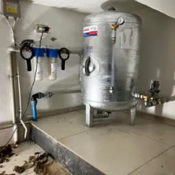 Hydrofor ze srebrnym zbiornikiem ciśnieniowym Wilmest ZCS/200/6, manometrem i filtrami wody, zainstalowany w pomieszczeniu technicznym z widocznymi śladami prac wykończeniowych na podłodze.