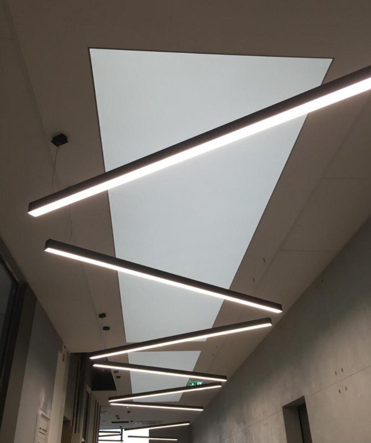 Nowoczesne oświetlenie liniowe LED na suficie podwieszanym w korytarzu biurowym, widok z dołu.