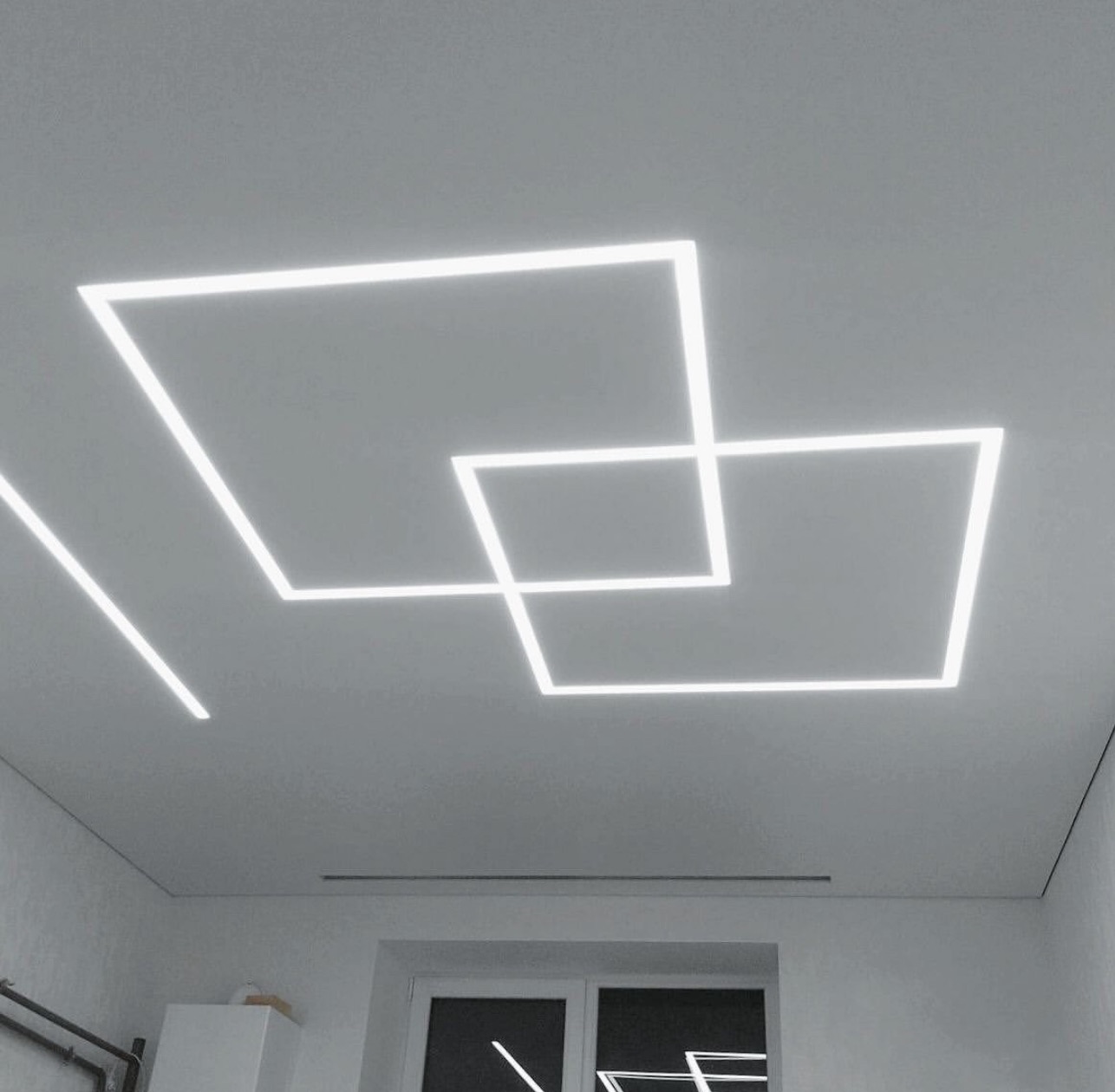 Nowoczesny sufit z geometrycznym oświetleniem LED w Chorzowie. Dwie przecinające się kwadratowe oprawy i pojedyncza linia świetlna, minimalistyczny design.