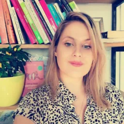 Portret kobiety z książkami w tle, możliwe, że psychoterapeutki. Widoczna roślina w doniczce i książka Stefanie Stahl 'Odkryj swoje wewnętrzne dziecko'.