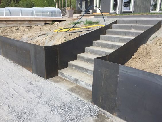 Schody zewnętrzne z szarej kostki, obramowane metalowymi panelami, prowadzące do domu z widocznym basenem pod plandeką w tle.