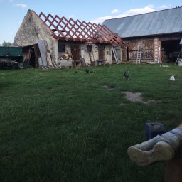 J.W.bud - Stary budynek gospodarczy z częściowo zdjętym dachem, widoczna więźba dachowa, na podwórku kury, w tle drabiny i sprzęt gospodarczy.