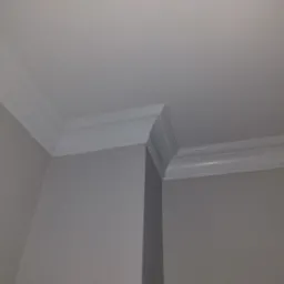 Wykończony narożnik sufitu i ścian z zamontowaną białą listwą dekoracyjną, widok od dołu.