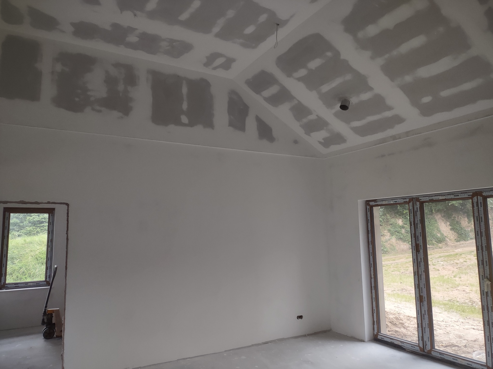 Wnętrze w trakcie remontu: sufit podwieszany z płyt gipsowo-kartonowych, częściowo zaszpachlowany, ściany przygotowane do malowania, widoczne okno i drzwi balkonowe.