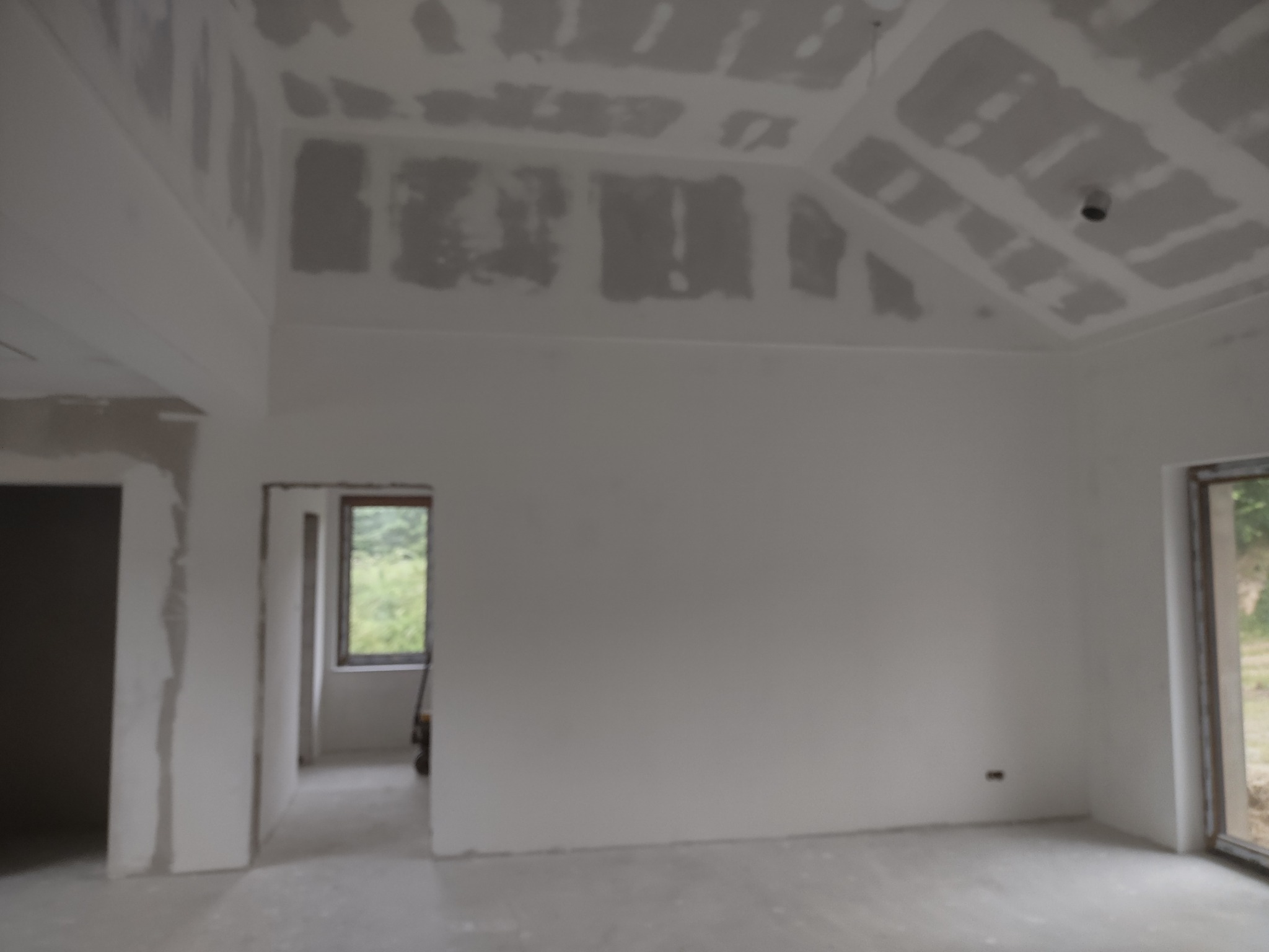 Wnętrze w trakcie wykończenia w Janowie Lubelskim: surowe ściany przygotowane do malowania, widoczne szpachlowane łączenia płyt gipsowo-kartonowych na suficie i ścianach, surowa podłoga, okno...