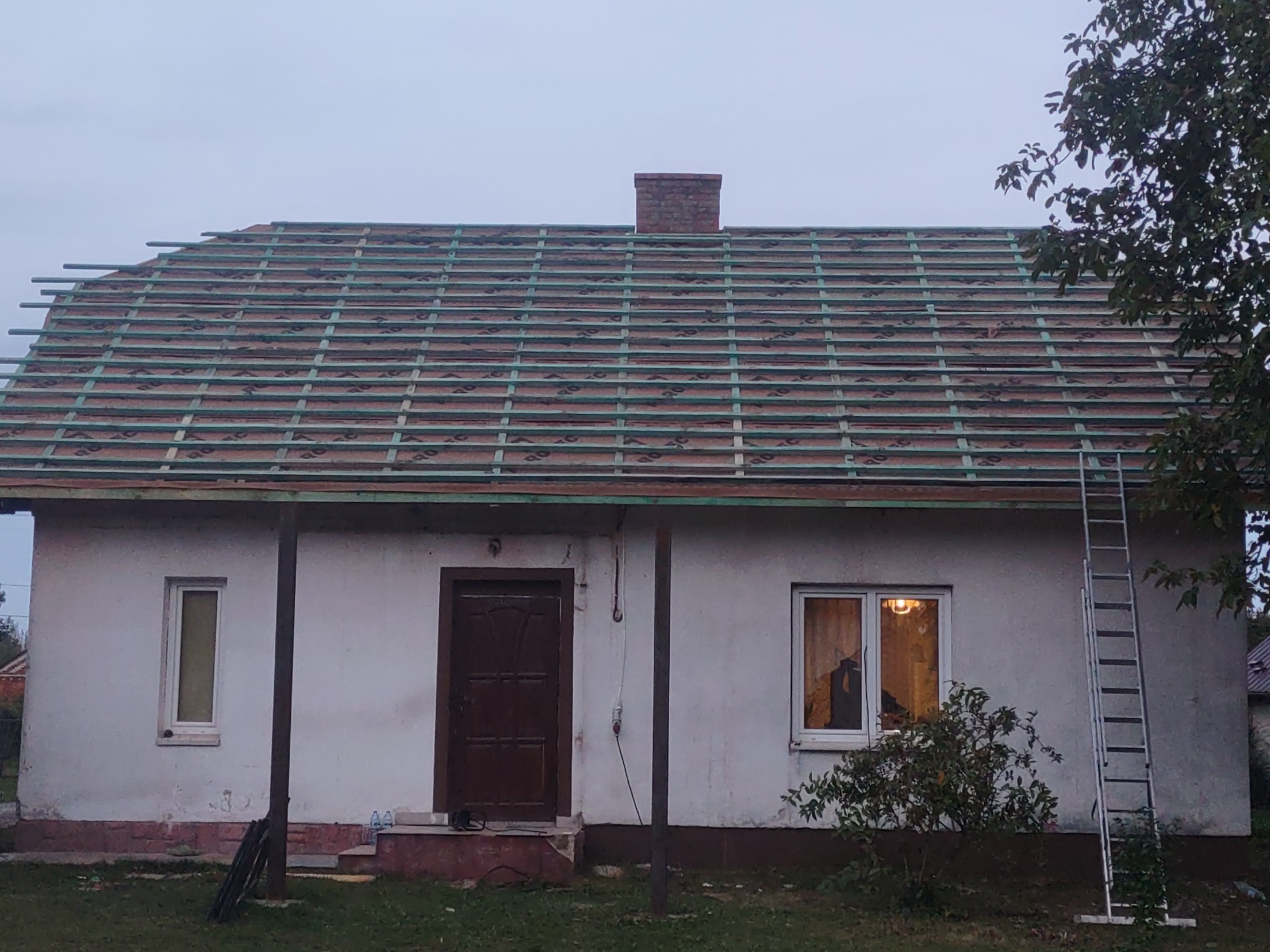 Dom jednorodzinny z widoczną konstrukcją drewnianą dachu przed położeniem pokrycia, drabina oparta o ścianę, ceglany komin.