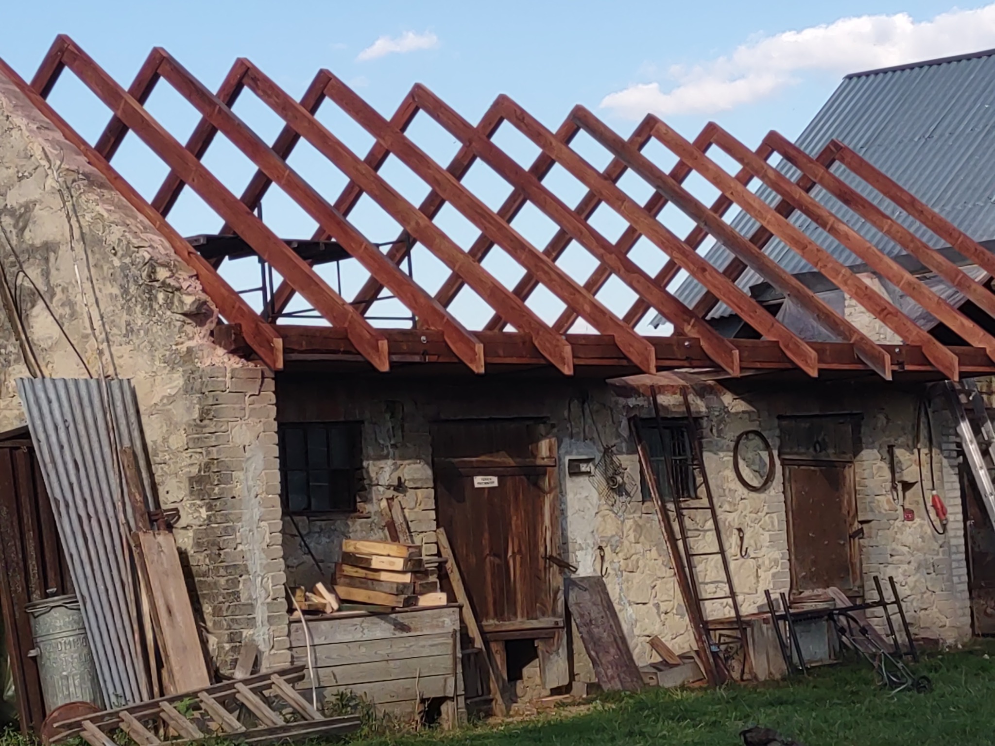 Konstrukcja nowej drewnianej więźby dachowej na starym, kamiennym budynku gospodarczym, widoczna drabina i narzędzia