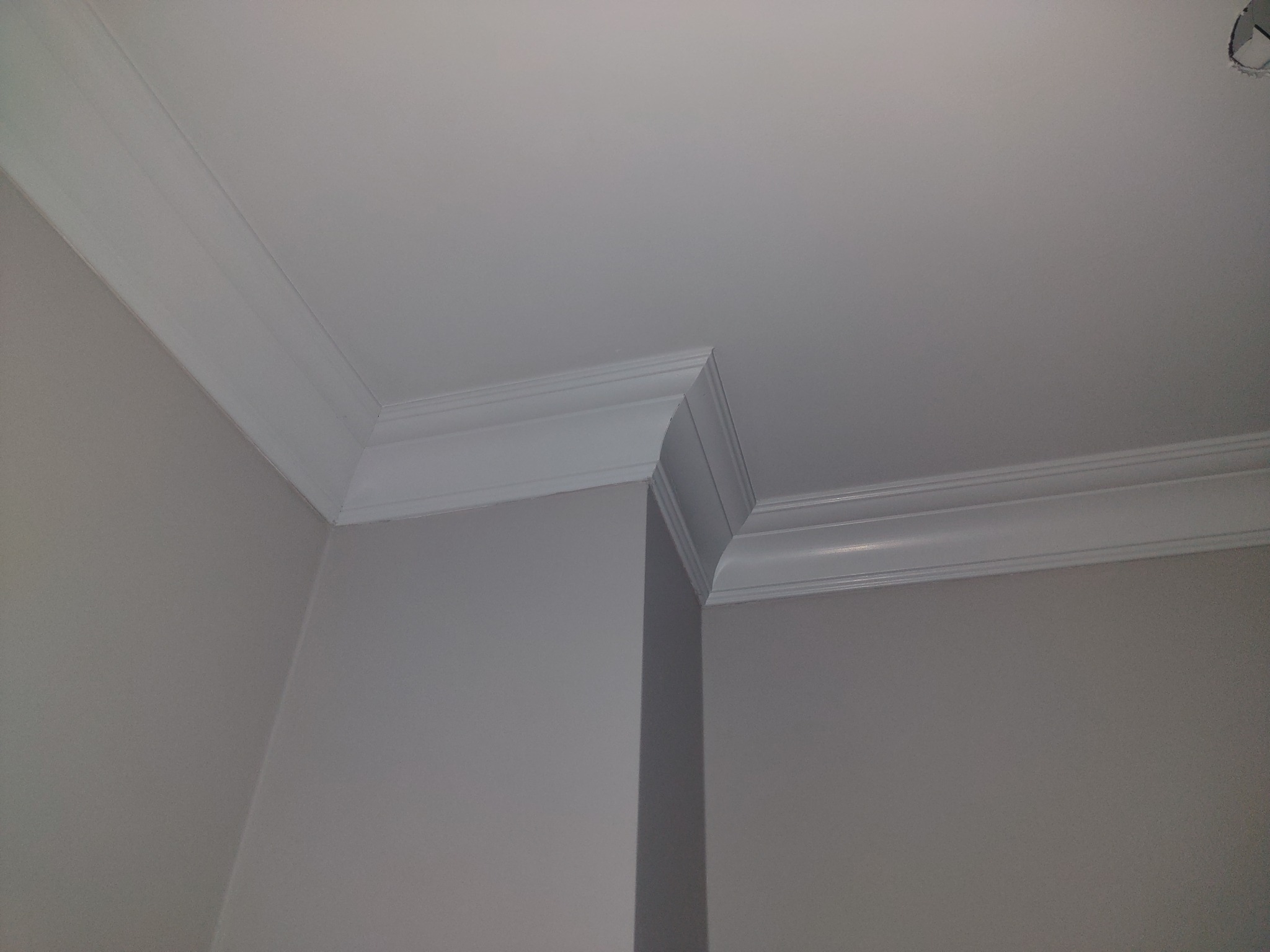Wykończony narożnik sufitu i ścian z zamontowaną białą listwą dekoracyjną, widok od dołu.