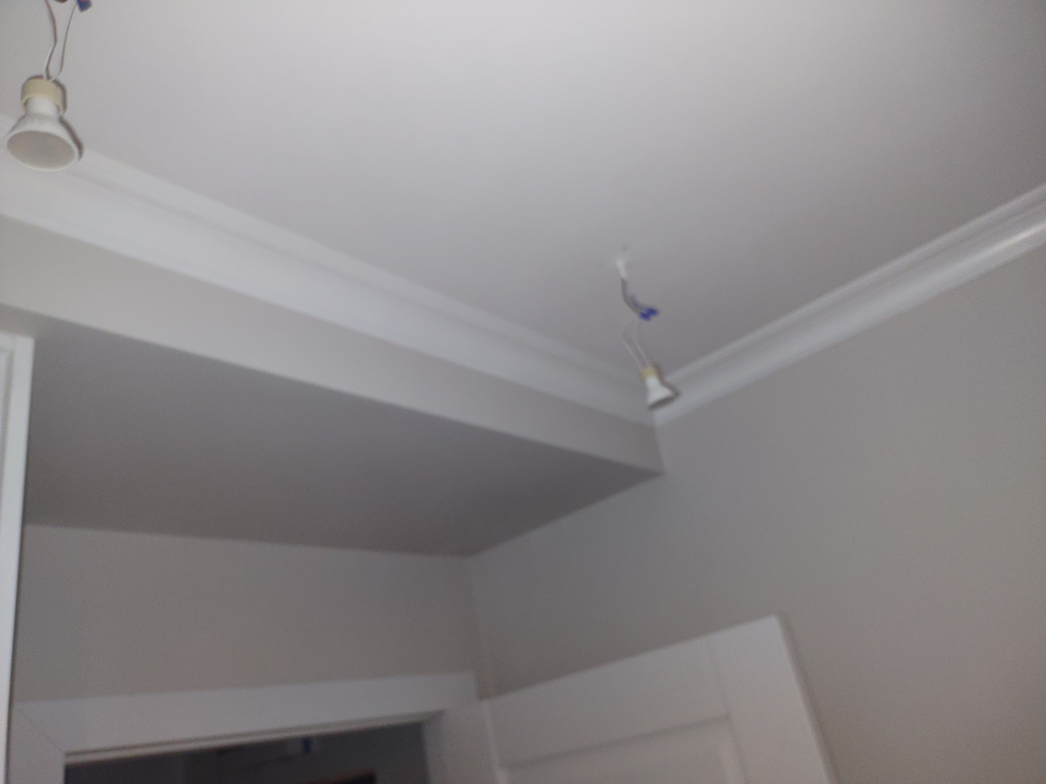 Wnętrze w trakcie prac wykończeniowych: biały sufit z listwami dekoracyjnymi i wiszącymi przewodami od lamp