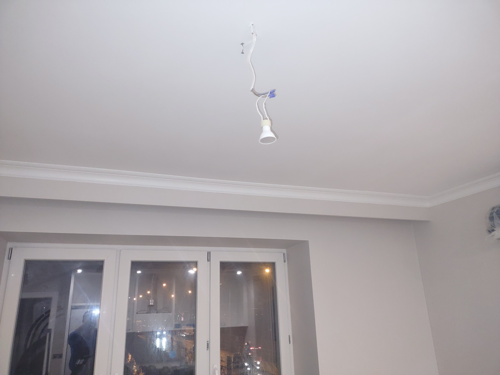 Biały sufit z listwą ozdobną i wiszącą żarówką na przewodach, widok na okno z odbiciem