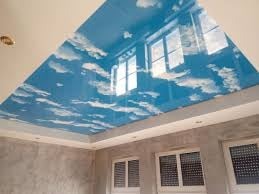 Niebieski sufit z nadrukiem chmur, odbijający światło z okien, widoczne szare ściany i oświetlenie punktowe.