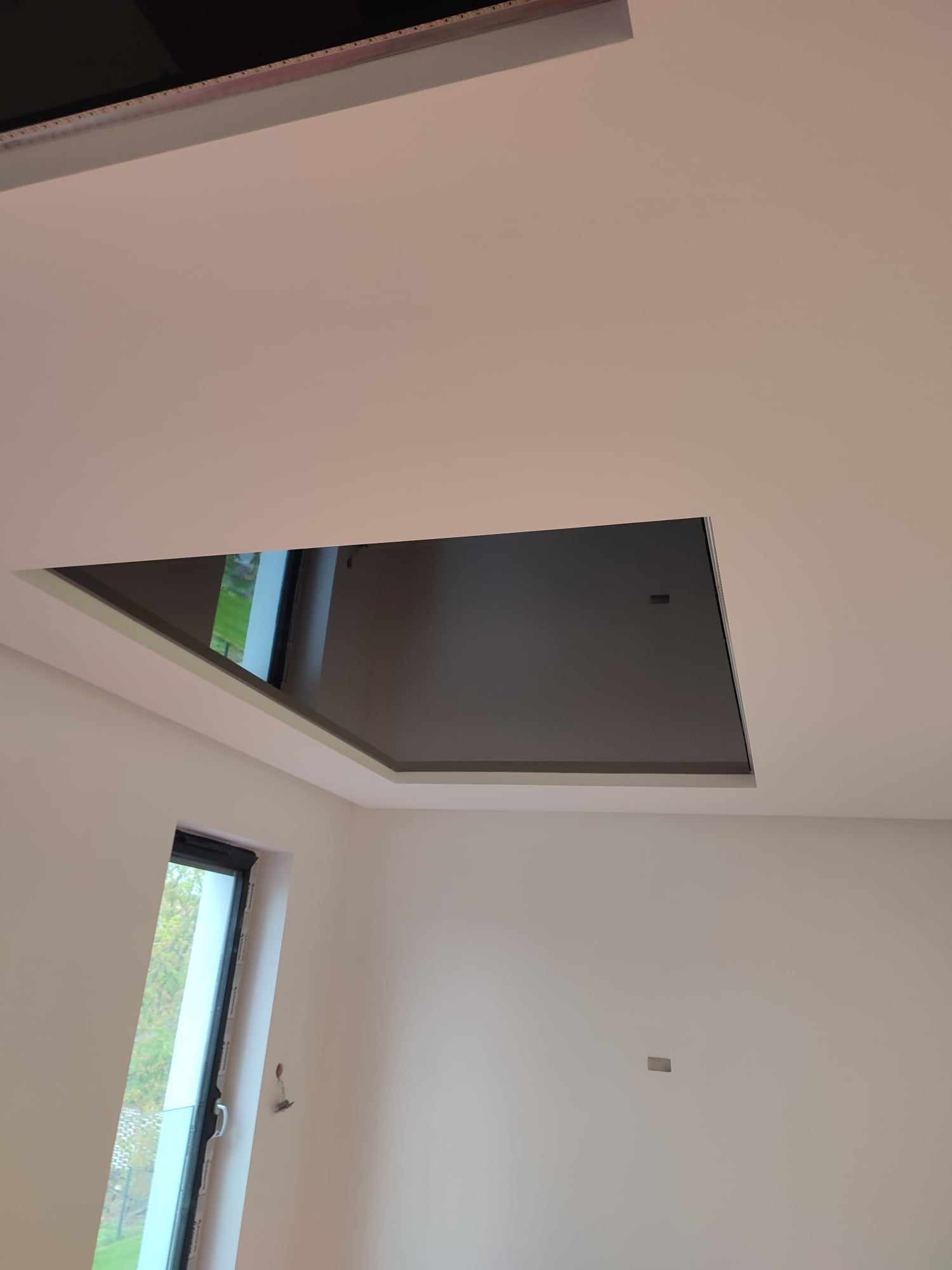 Nowoczesny sufit z wnęką, pomalowany na biało, z widocznym oknem dachowym i fragmentem okna ściennego.