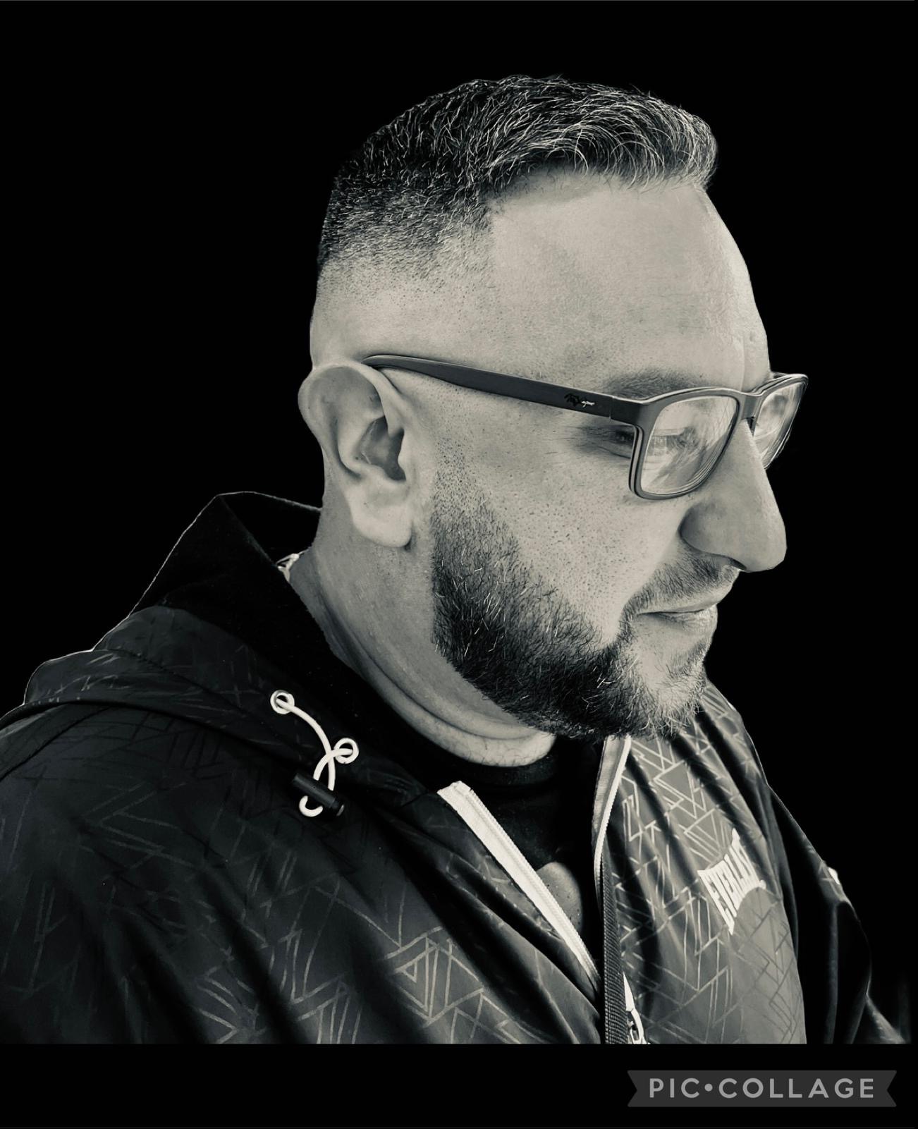 Mężczyzna z krótką, cieniowaną fryzurą i brodą, w okularach, profil, czarno-białe zdjęcie.