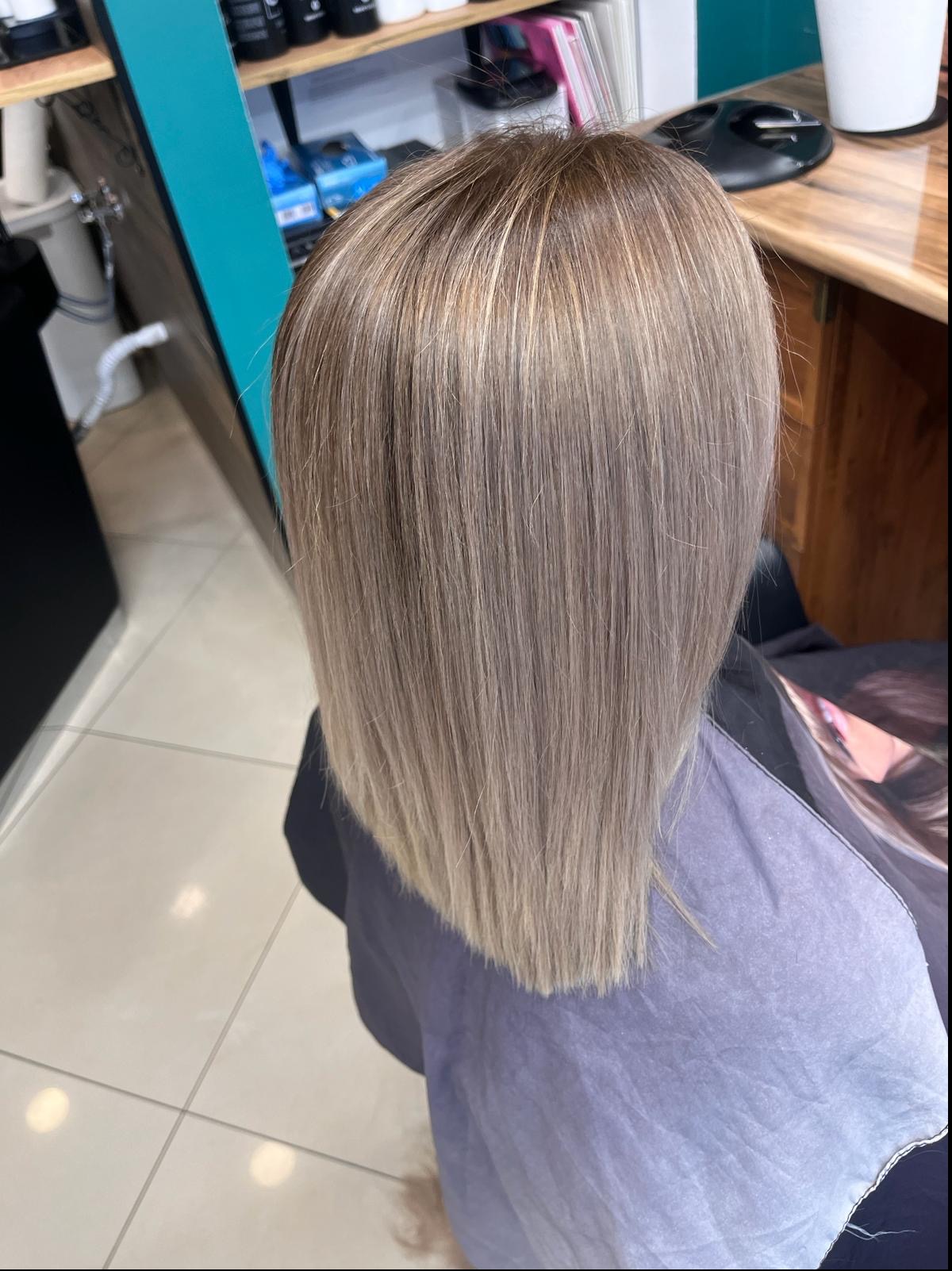 Świeżo ostrzyżone, proste włosy w odcieniach blondu i brązu, widoczne od tyłu, z peleryną ochronną w salonie.