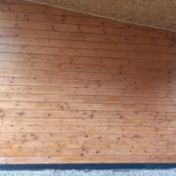 Ściana altany z desek boazeryjnych, widoczne sęki i naturalne usłojenie drewna, podbitka dachowa z płyty OSB.