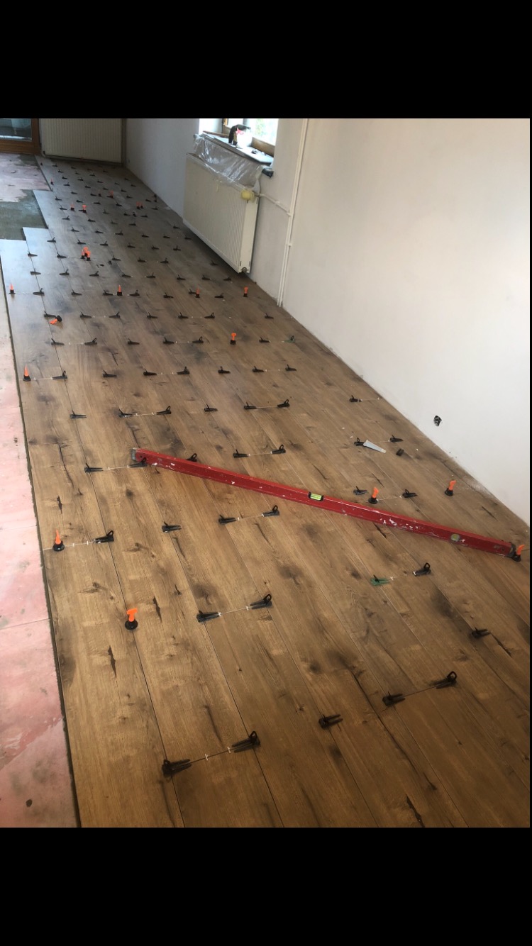 Układanie paneli podłogowych z użyciem systemu poziomowania, widoczna poziomica laserowa i kliny dystansowe.