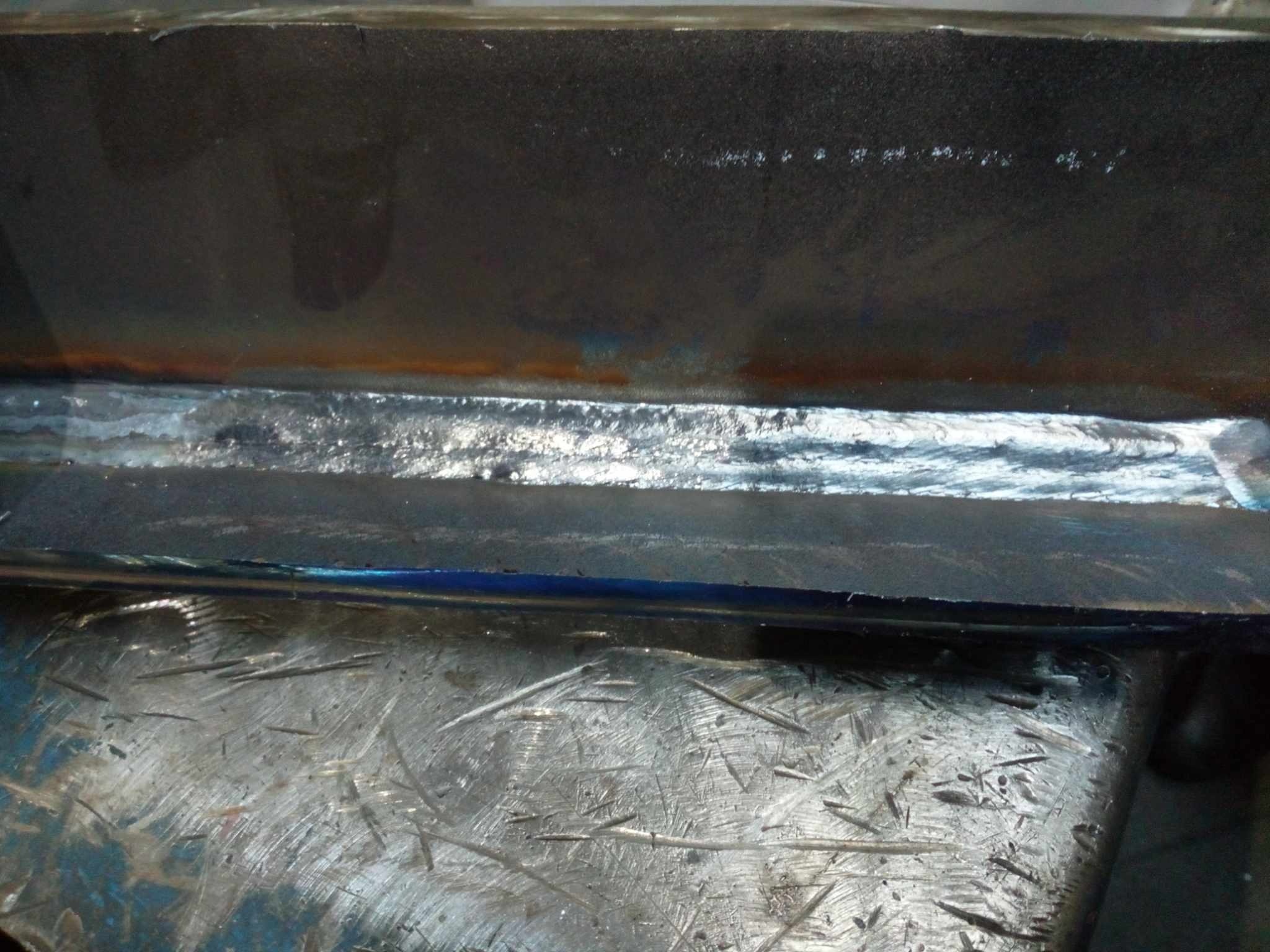 Spoina łącząca dwa elementy stalowe, wykonana w Zielonej Górze, widoczna na tle metalowego stołu warsztatowego z licznymi śladami użytkowania.