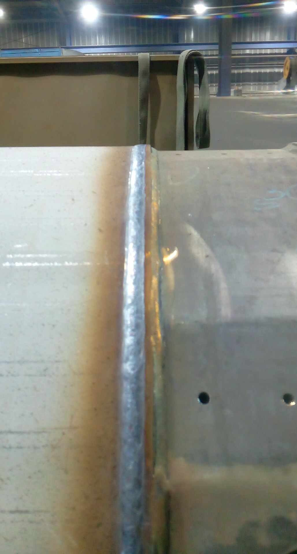 Spoina na metalowej rurze, widoczne przebarwienia termiczne i otwory montażowe, w tle elementy konstrukcyjne hali.